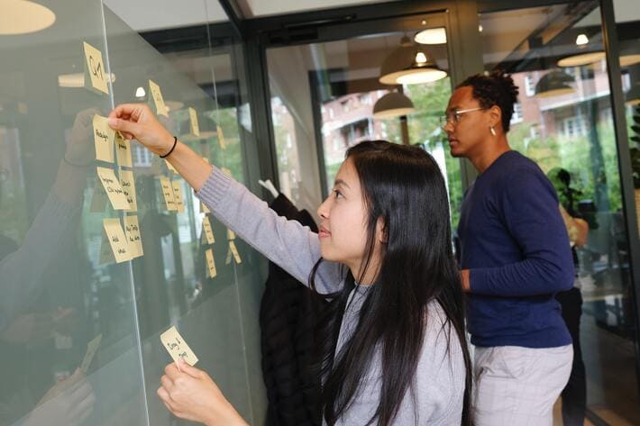 A girl and a boy are writing and pasting stickers on a chalkboard inside the marketing office to plan media activities.