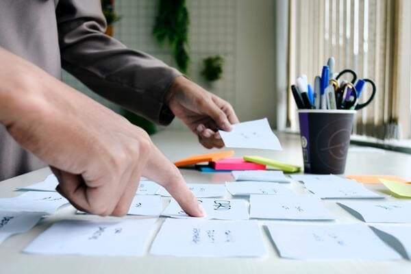 A person writing on a piece of paper and arranging them in the right sequence to set up a business process.